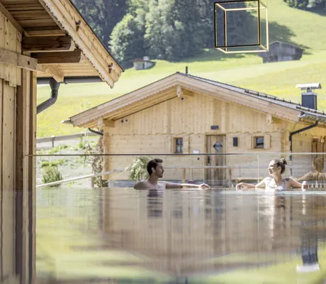Eine Frau und ein Mann entspannen im Outdoorpool der Hygna Chalets