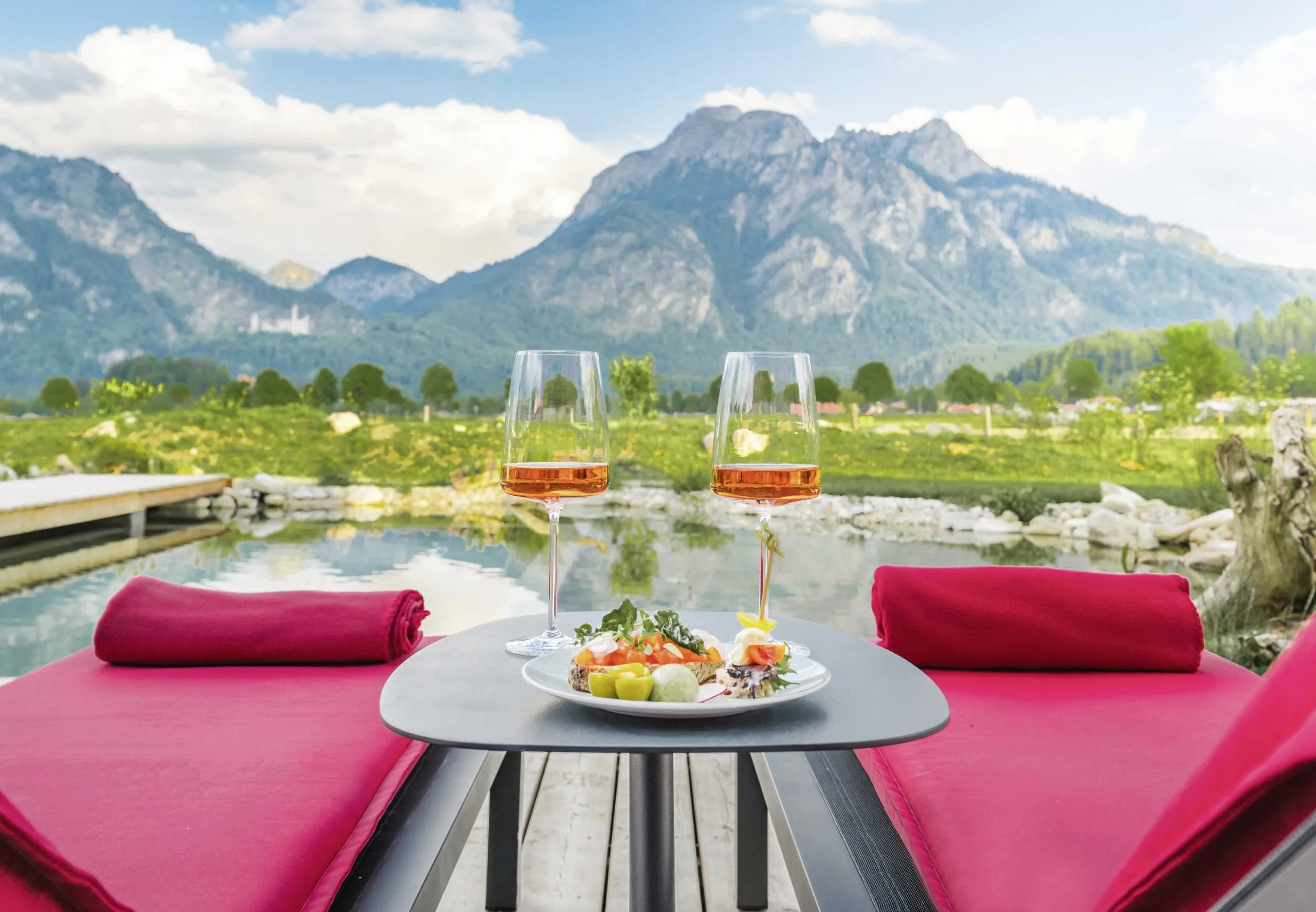 rot gepolsterte Liegen und Tisch mit zwei ros&eacute;farbenen Getr&auml;nken im Das R&uuml;bezahl am Naturbadeteich