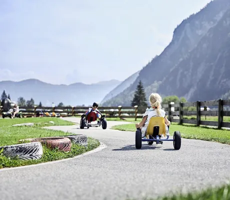 Go Card fahrende Kinder in Rückenansicht am Ufer des Achensees des Familienresort Buchau