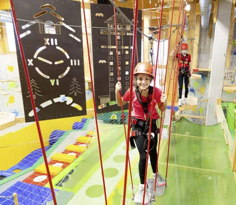 Zwei Mädchen mit Helmen und Sicherungsgurten im Indoor-Kletterparcours