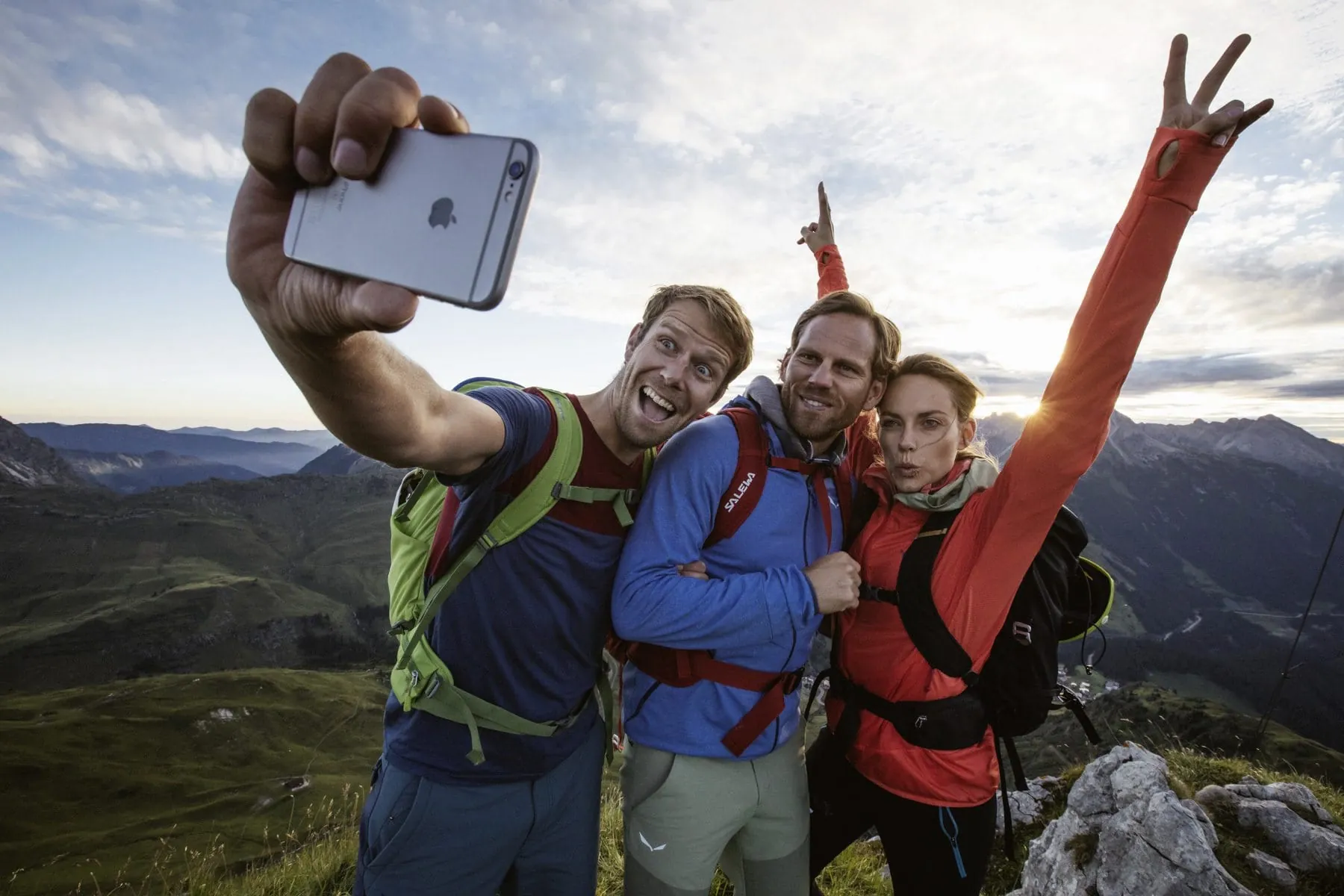 Drei Bergwanderer, zwei M&auml;nner und eine Frau, fotografieren sich auf dem Gipfel mit Victory-Zeichen