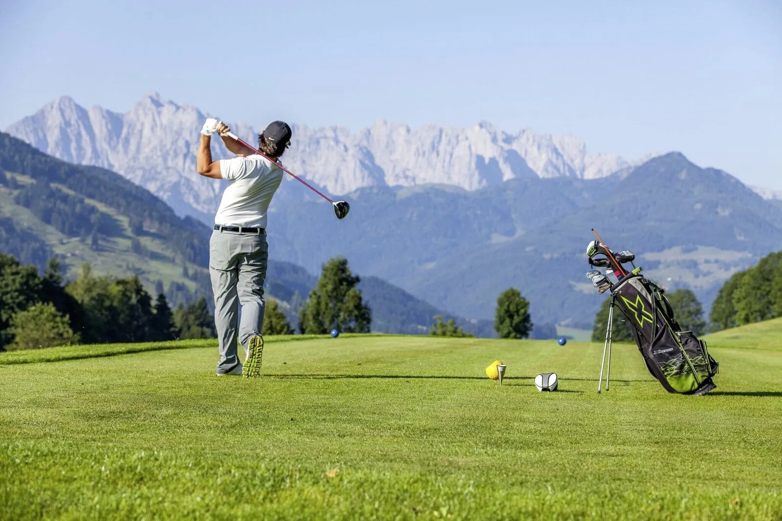 Golfer in R&uuml;ckenansicht beim Abschlag mit Bergblick im Peternhof Wohlfuehlresort
