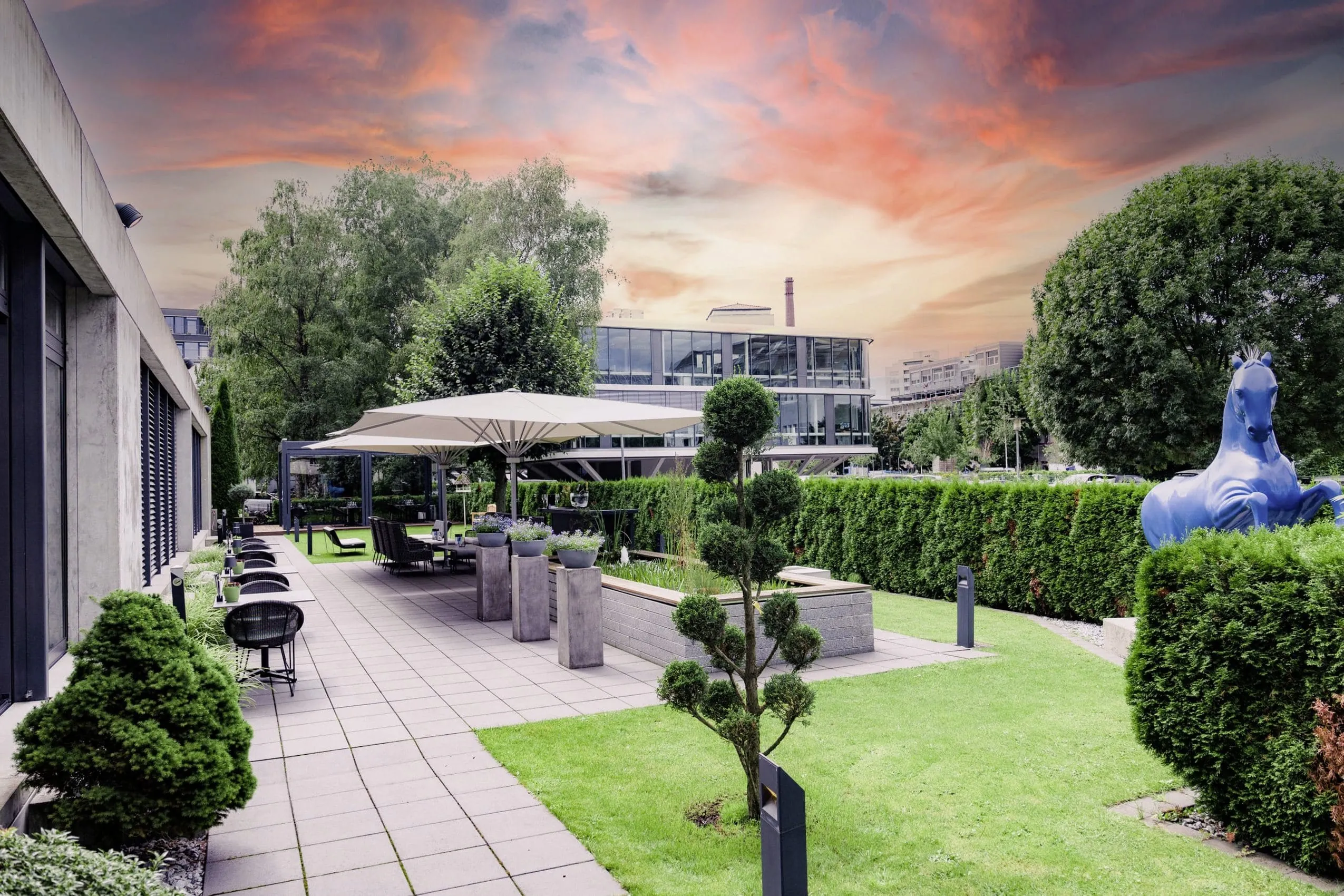 Blick in den Garten des Hotel Der Blaue Reiter mit vom Sonnenuntergang rot gefärbten Wolken im Hintergrund