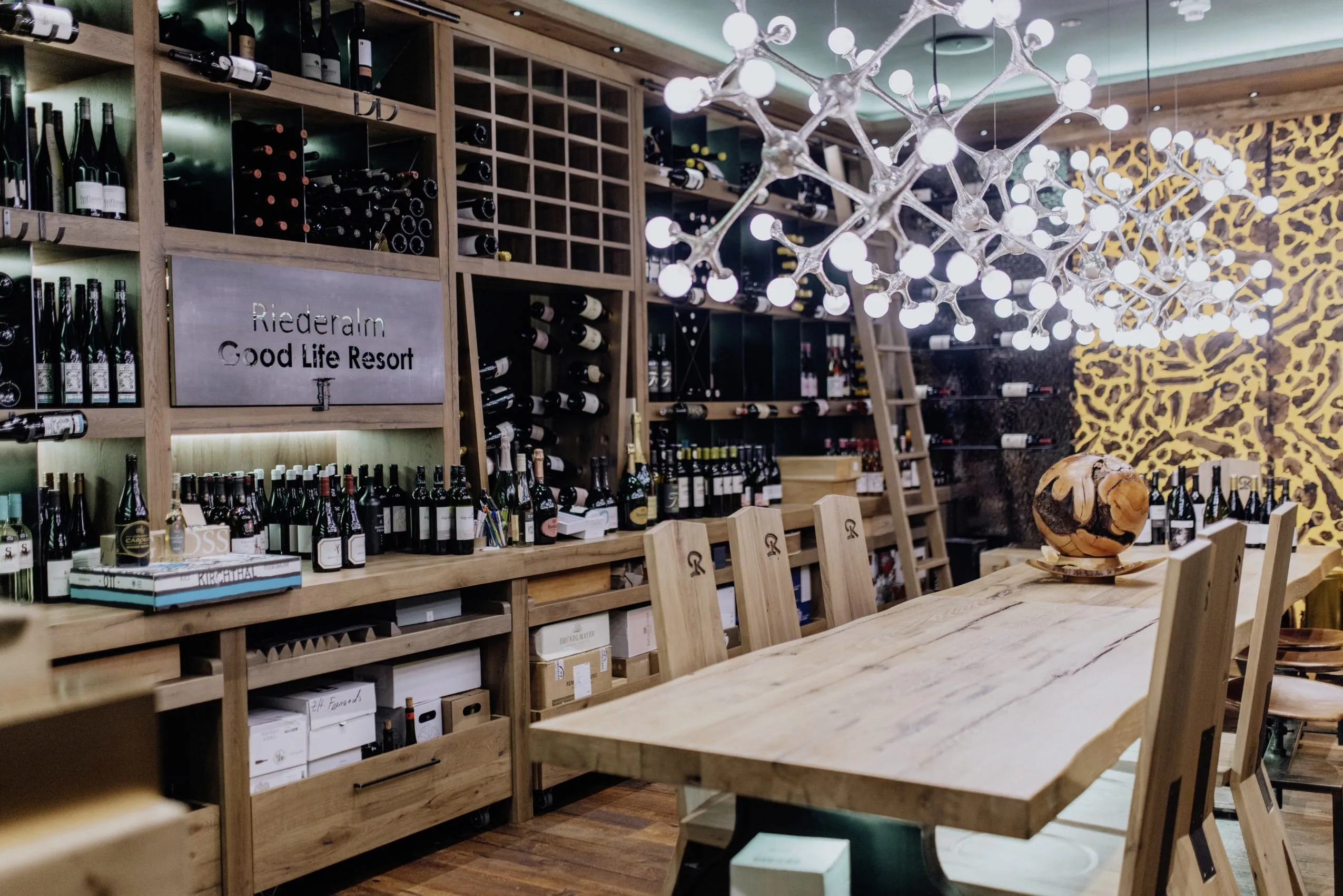 Vinothek im Good Life Resort Riederalm mit mehrarmigem modernem Leuchter &uuml;ber dem Holztisch