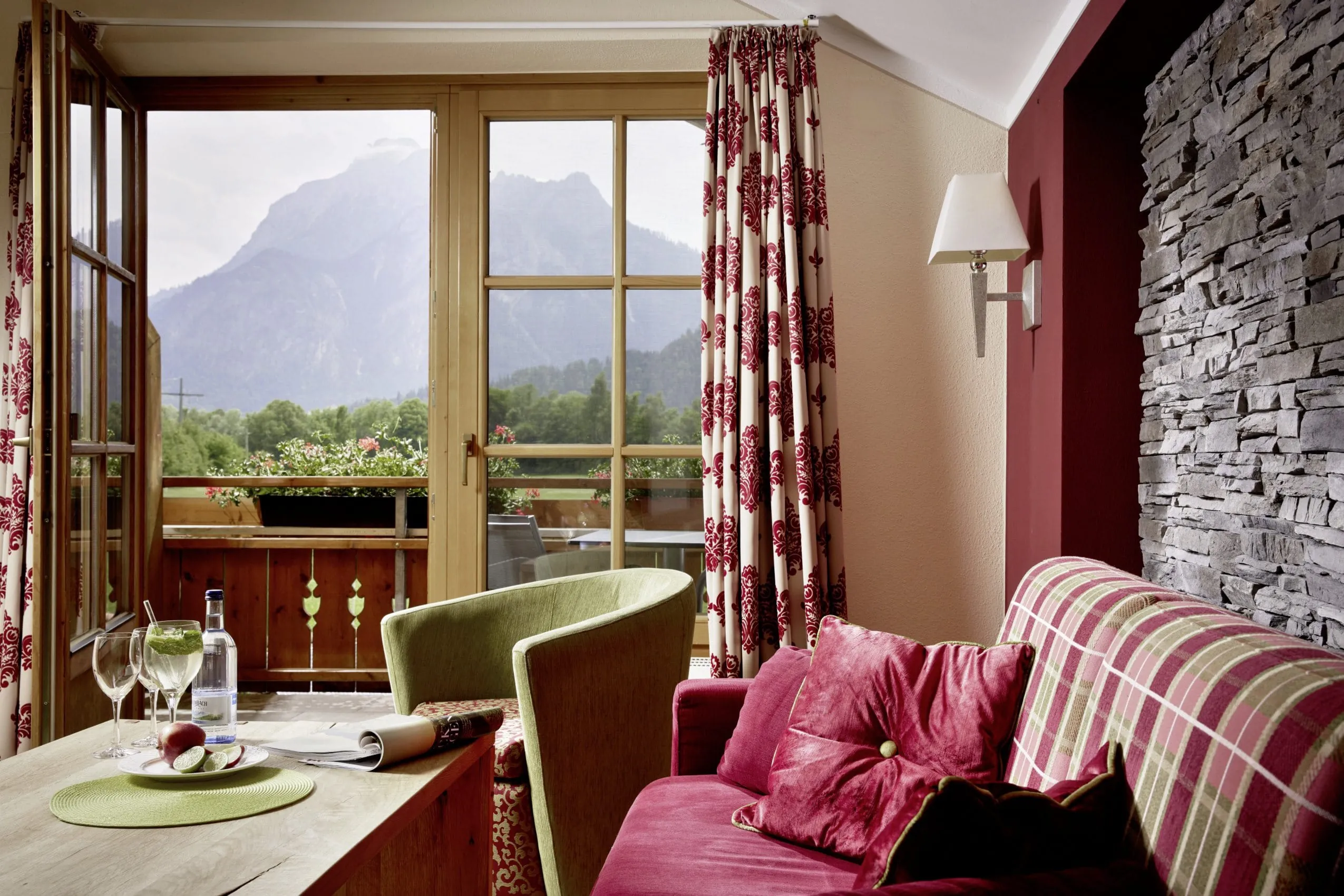Stilvolll eingerichtetes Zimmer im alpinen Stil in Rot- und Gr&uuml;nt&ouml;nen im Wellnesshotel Sommer mit Balkon und Blick in die Berge