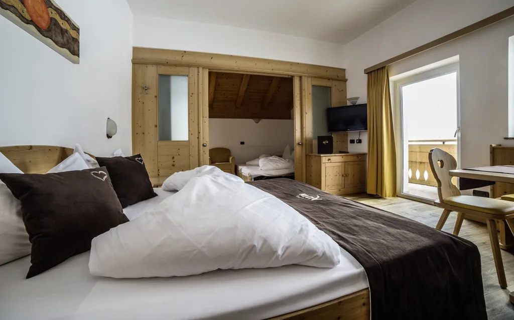 Familienzimmer mit modernem Holzbett, klassisch alpiner Tischbestuhlung und Nebenzimmer im Hotel Alpin