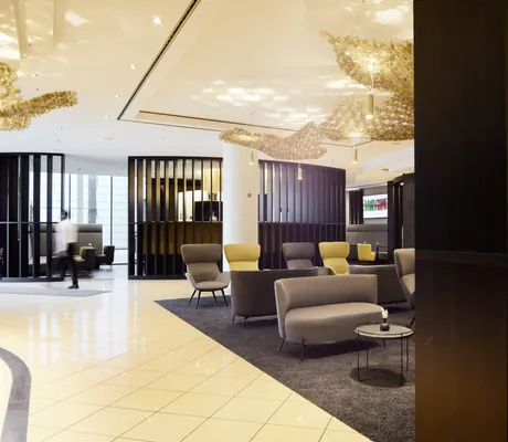 Lobby im Hotel Esperanto mit großem goldenen Deckenleuchter und grauenen und beigen Sitzmöbeln