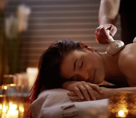 Frau erhält Kräuterstempelmassage bei Kerzenschein im Hotel Esperanto