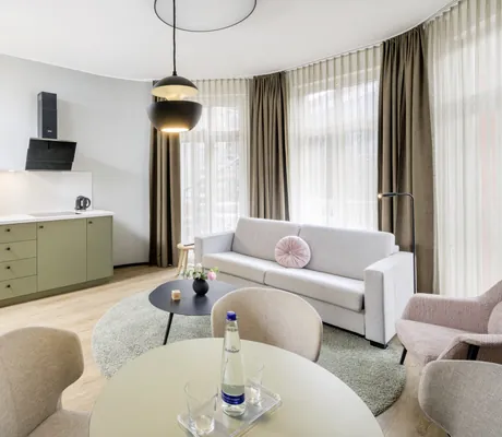 Apartment in skandinavischem Design in Rosé-Beigetönen mit Kitchenette und Sofa vor bodentiefen Fenstern im KOOS Hotel & Apartments