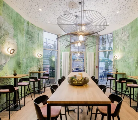 Bar „KOOS Bowls & Bar“ in skandinavischem Design und grüner Blumentapete mit bodentiefen Fenstern zum Innenhof im KOOS Hotel & Apartments