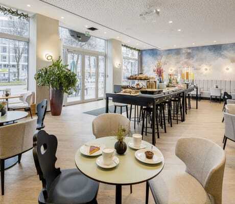 Restaurant „KOOS Bowls & Bar“ mit bodentiefen Fenstern, in skandinavischem Design mit beiger Bestuhlung und mittigem Frühstücksbuffet im KOOS Hotel & Apartments in München