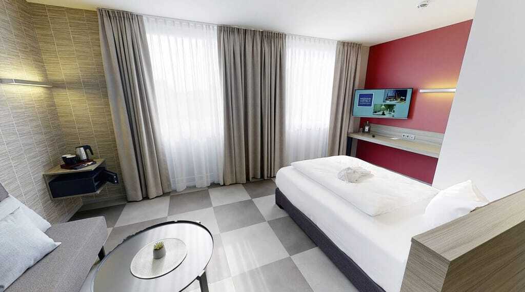 Zimmer mit Einzelbett, Schachbrettboden, beigen Vorhängen und roter Wand