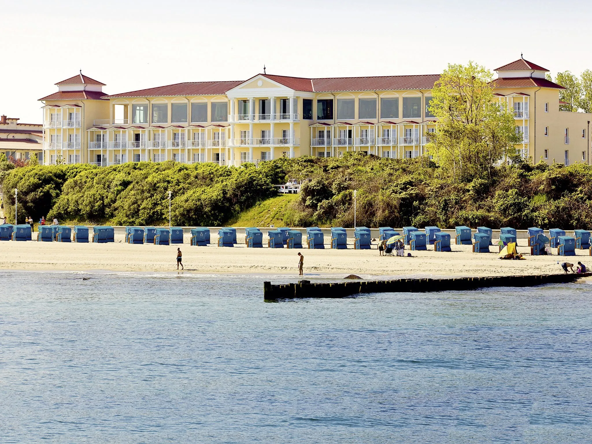 Außenansicht des MORADA Strandhotel mit blauen Strandkörben am Strand