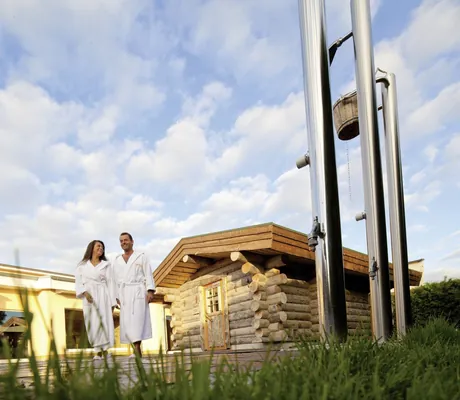 Paar in weißen Bademänteln vor der Blockhaussauna des MORADA Strandhotel