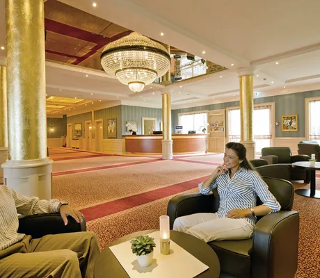 Paar sitzt in den dunklen Ledersesseln vor dem Kronleuchter der Lobby im MORADA Strandhotel