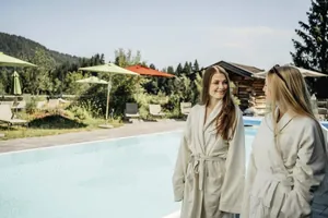 Zwei Frauen in Bademänteln lächeln sich vor dem Outdoorpool des Hotel Oberstdorf an