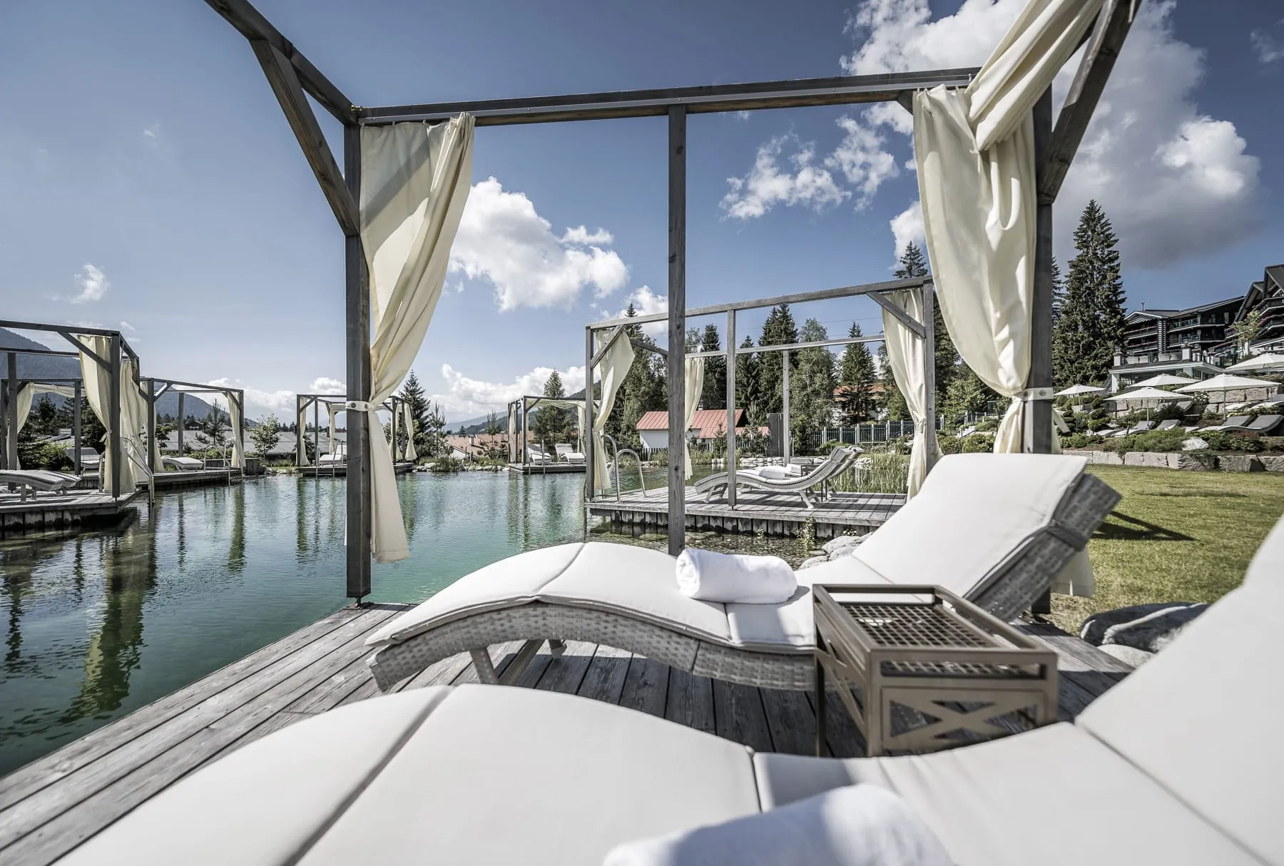 Naturbadeteich im Garten des Alpin Resort Sacher Seefeld &ndash; Tirol mit einzelnen Ruheinseln mit Vorh&auml;ngen