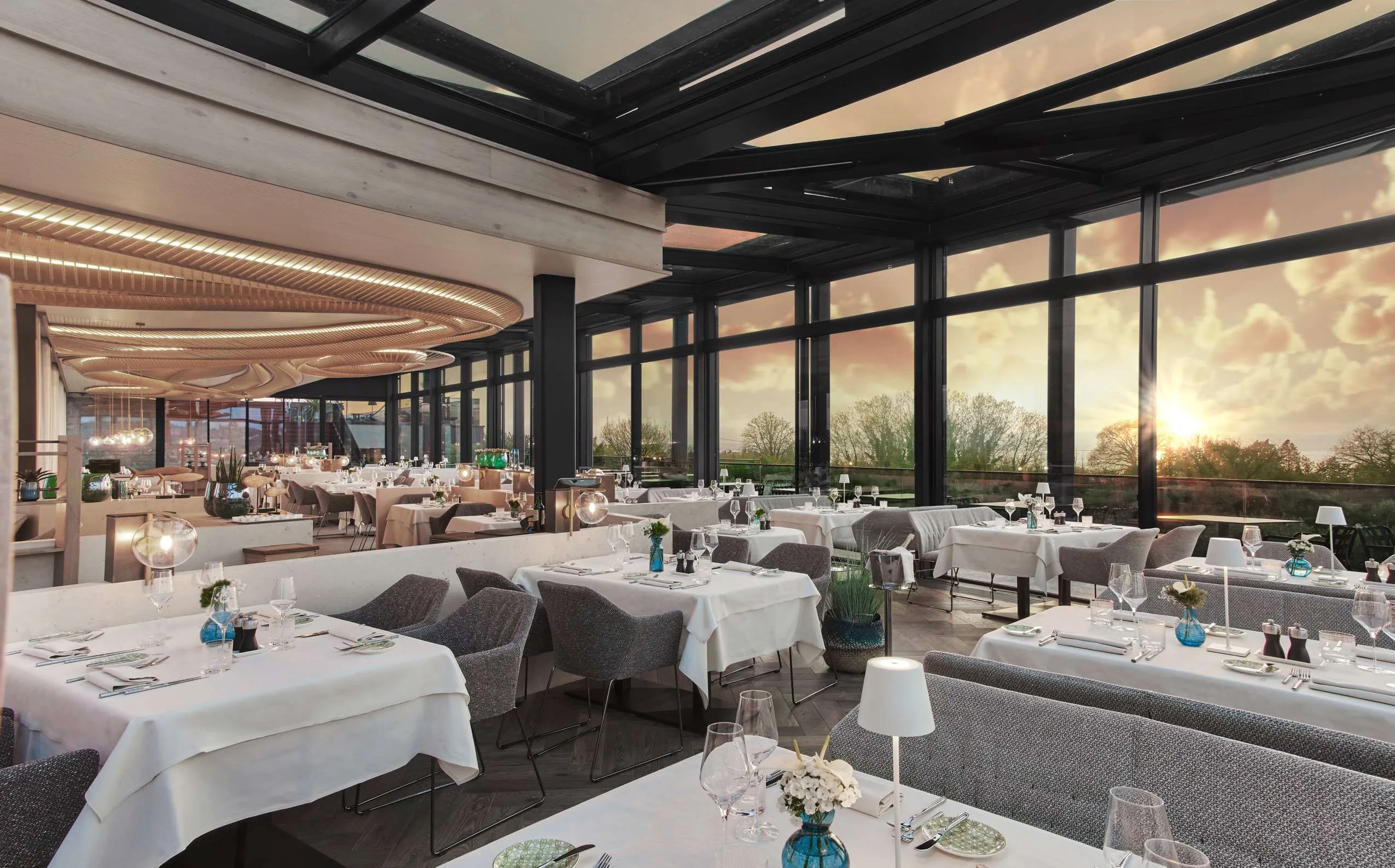 Panoramarestaurant mit eingedeckten Tischen, bodentiefen Fenstern und Blick auf den Gardasee bei Sonnenuntergang im Quellenhof Luxury Resort Lazise