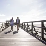 Zwei junge Menschen laufen in sommerlicher Kleidung über den Steg am Strand von St. Peter-Ording