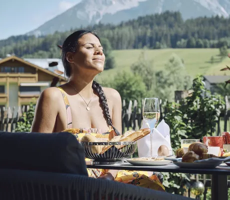 dunkelhaarige Faru mit Zopf genießt mit geschlossenen Augen das Frühstück auf der Terrasse