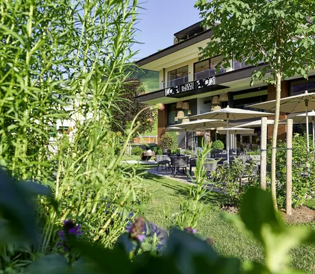 Blick vom Garten auf die Terrasse mit beigen Sonnenschirmen in die HOCHKÖNIGIN