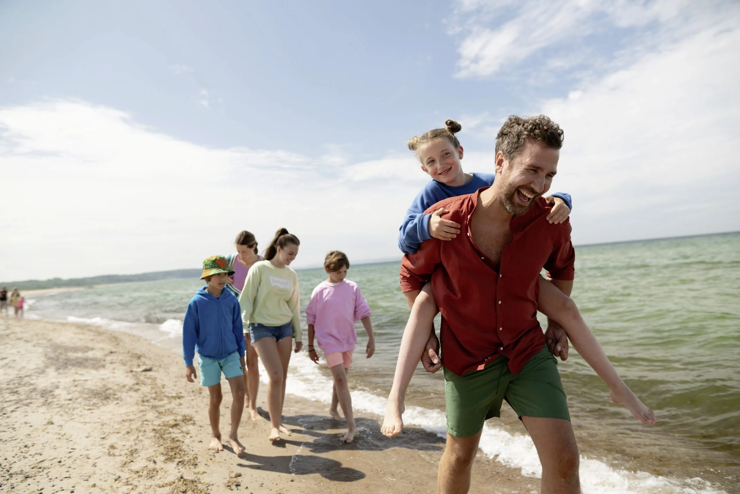 Familie mit Eltern und Kindern läuft am Sandstrand vor der Ostsee entlang