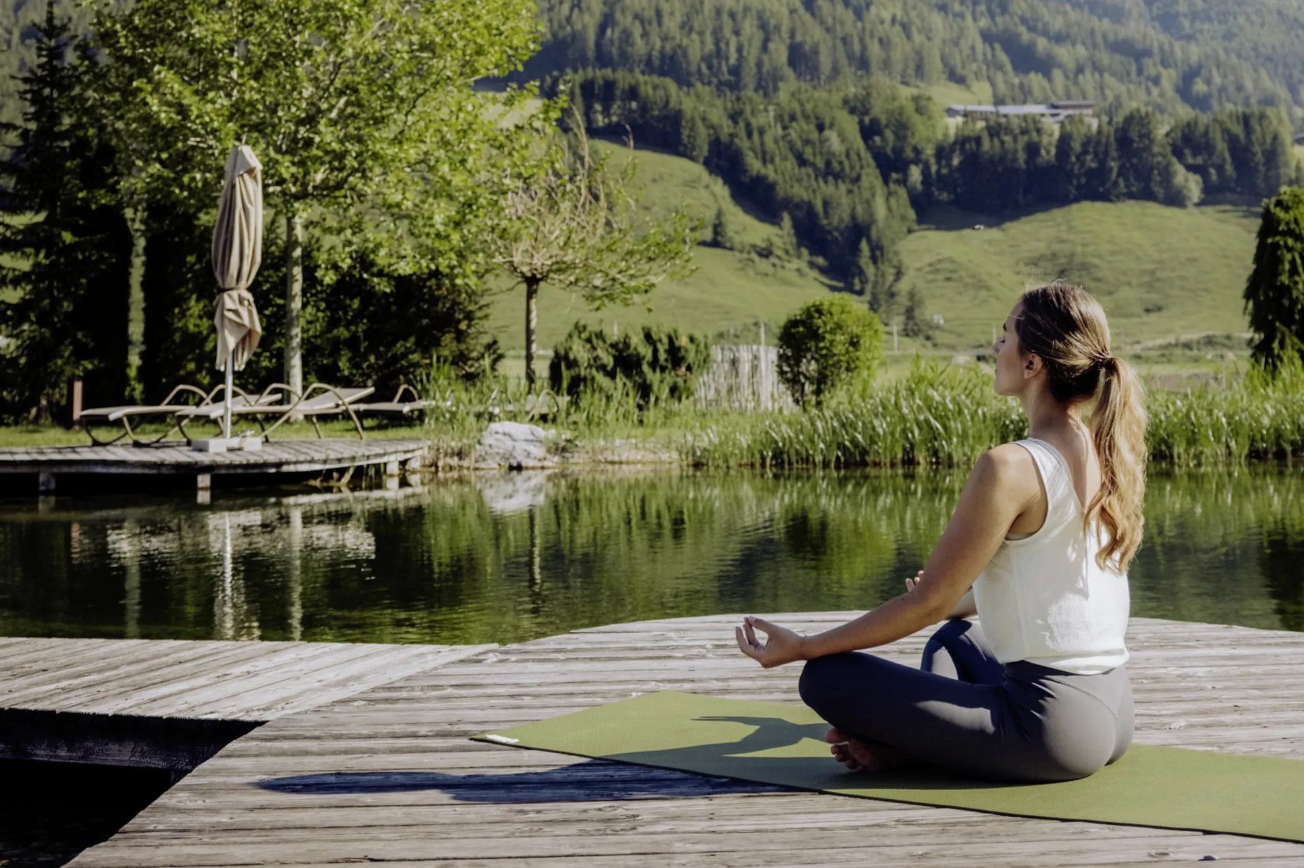 Meditierende Frau im Schneidersitz auf Holzplattform im Natursee des Naturresort PURADIES