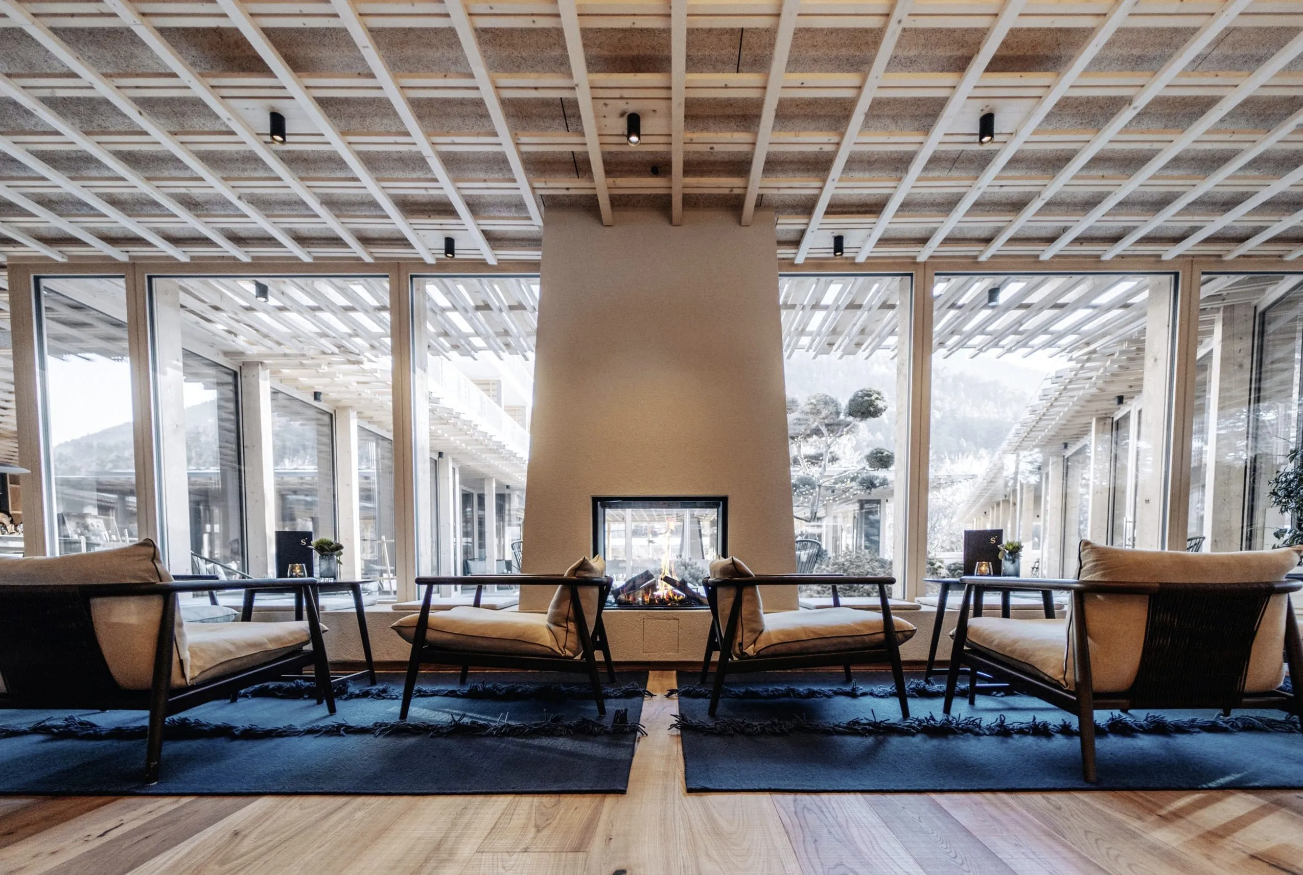 Lobby mit Sesseln, offenem Kamin und Blick auf das begr&uuml;nte Atrium im Sensoria Dolomites