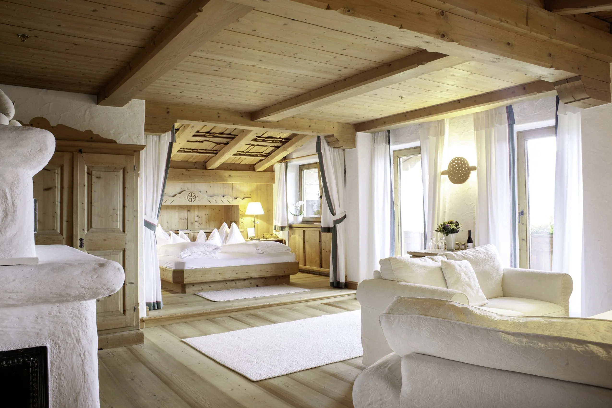 Suite im Landhausstil mit Holzboden- und -decke, gemauertem Kachelofen und wei&szlig;em Stoffsofa im Stanglwirt