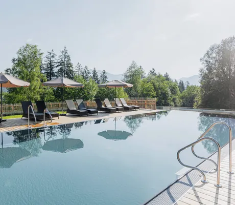 Outdoor-Infinitypool des Lechlife Travelhouse mit Liegen und Blick auf die umgebende Berglandschaft