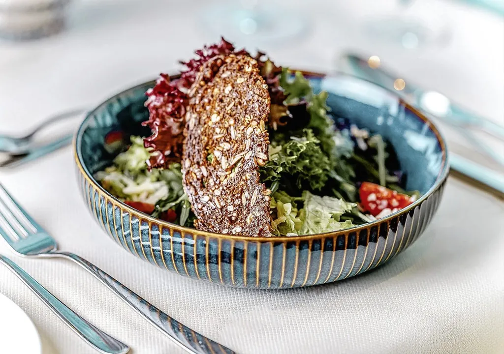 Lecker angerichteter Salat mit gerösteter Vollkorn-Brotscheibe in blauem Keramikteller im Restaurant des Hotels DAS AHLBECK Hotel & Spa