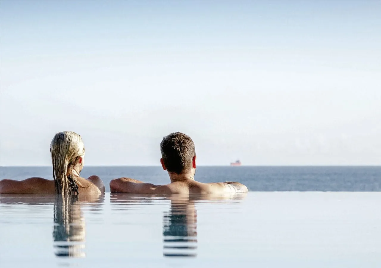 Mann und Frau entspannen im Outdoor-Infinitypool des Strandhotel DAS AHLBECK Hotel & Spa mit Blick auf die Ostsee