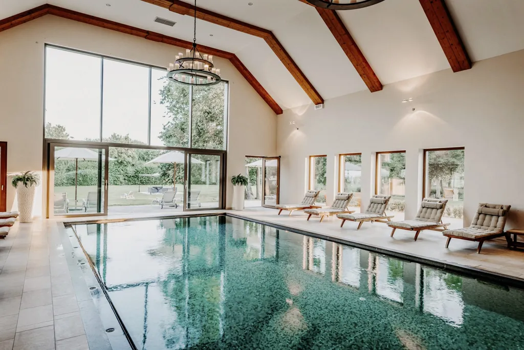 L&auml;ngsrechteckiger Innenpool mit t&uuml;rkisem Wasser, Liegen und L&uuml;ster vor bodentiefer Fensterfront