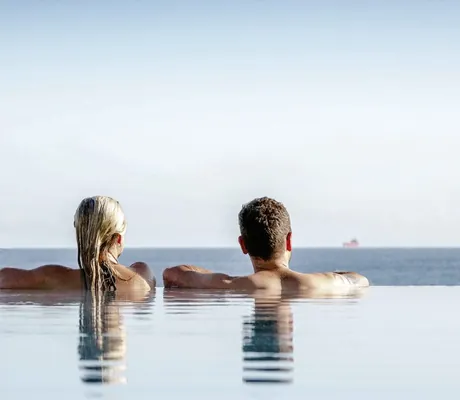 Mann und Frau entspannen im Outdoor-Infinitypool des Strandhotel DAS AHLBECK Hotel & Spa mit Blick auf die Ostsee