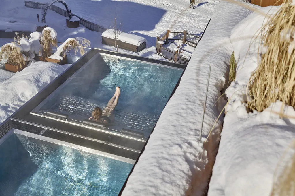 Frau liegt im vom Schnee umgebenen Outdoorpool des Hotel die HOCHKÖNIGIN