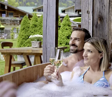 Paar im privaten Outdoor Badezuber der Alpin Chalets Oberjoch mit Sektglas in der Hand