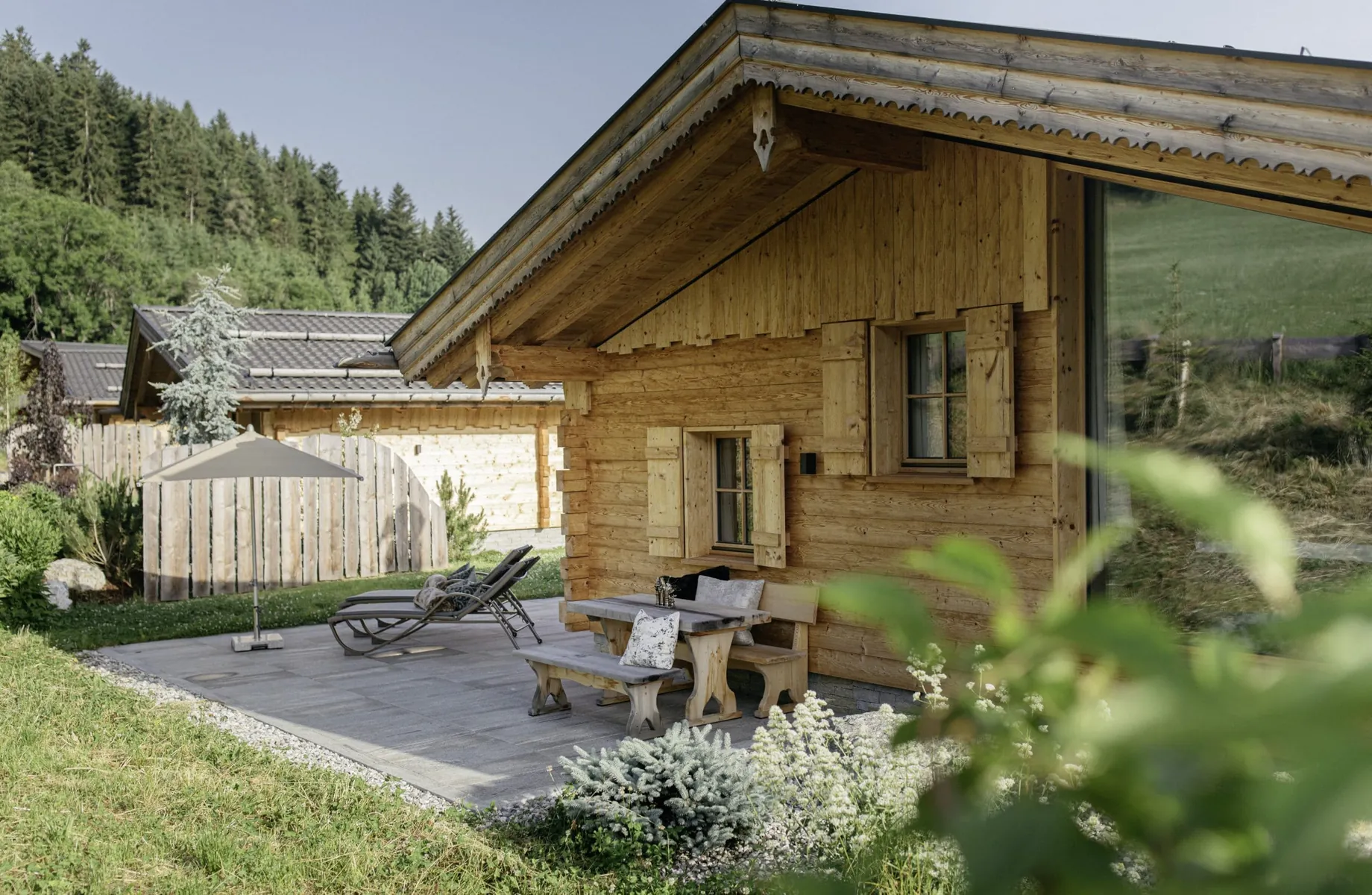 Blick auf eines der Hygna Chalets mit Sitzbank, Liegestühlen und Schirm auf Terrasse
