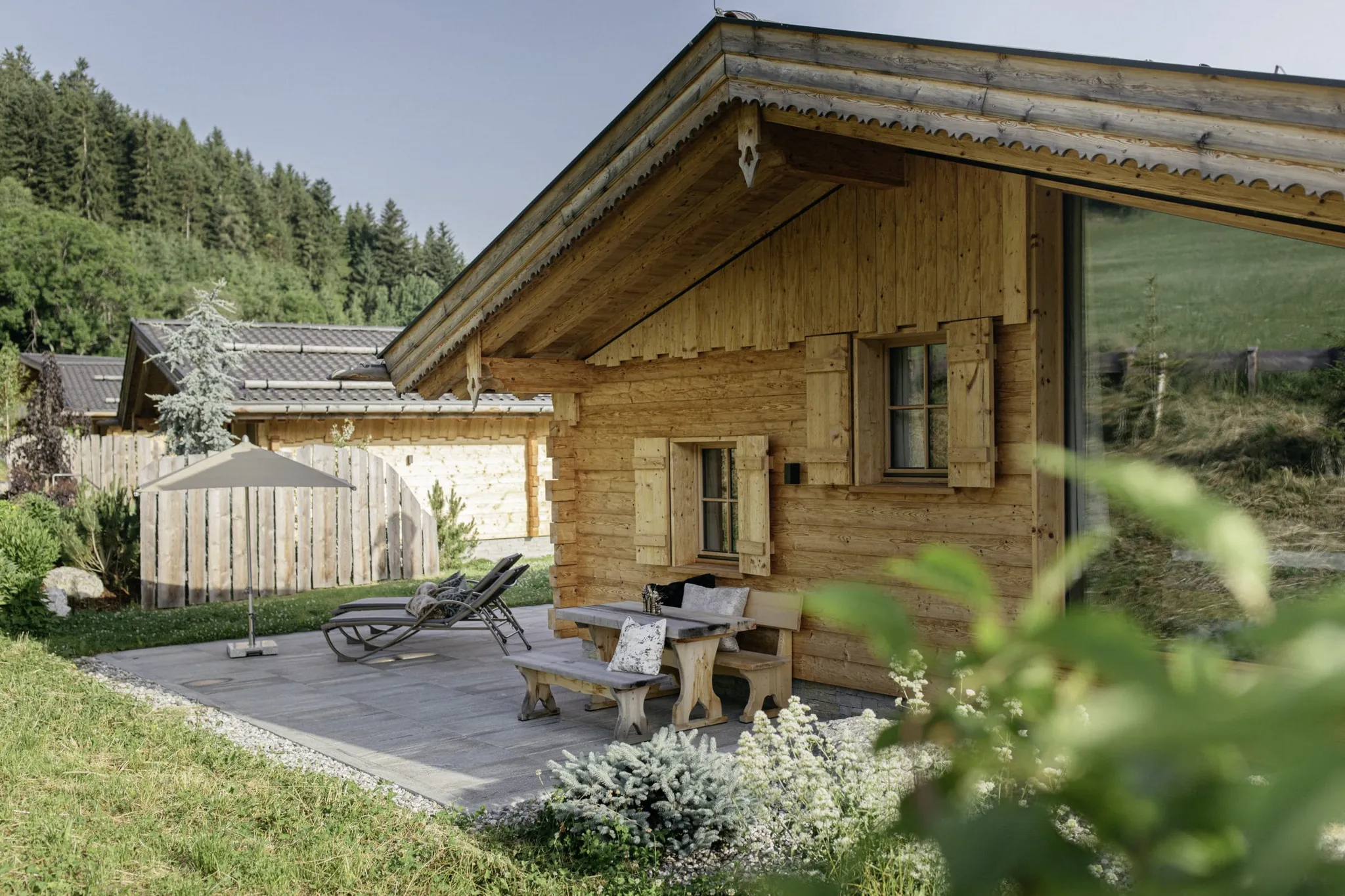Blick auf eines der Hygna Chalets mit Sitzbank, Liegestühlen und Schirm auf Terrasse