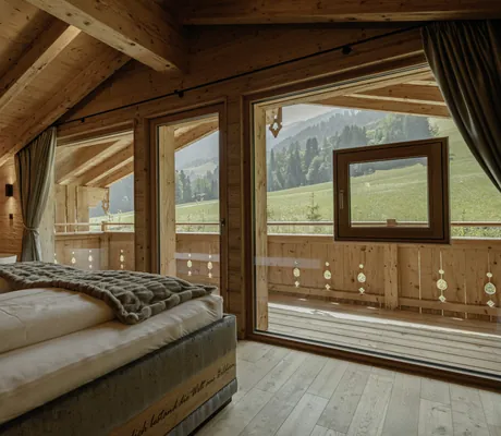 Schlafbereich der Hygna Chalets mit Doppelbett, Badewanne im Hintergrund und Blick in die grüne Natur