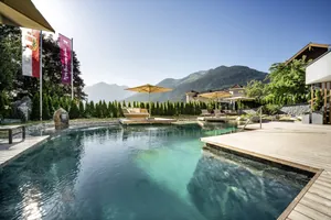 Naturpool des Hotel Gassner mit Sonnenliegen und -schirmen und Blick auf die Berge