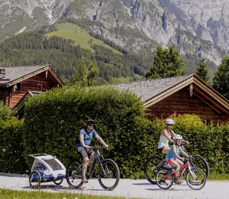 Familie fährt Fahrrad auf dem Gelände des Naturresort PURADIES mit Bergen im Hintergrund