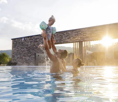 Vater wirft Tochter mit Schwimmflügeln in die Luft im Pool des Familotel Schreinerhof