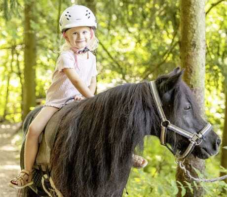 blondes Mädchen mit Helm sitzt auf schwarzem Pony im Familotel Schreinerhof