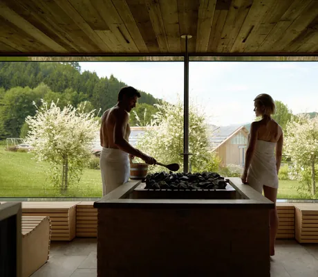 Pärchen mit weißen Frotteetüchern steht am Fenster in der Sauna des Familotel Schreinerhof