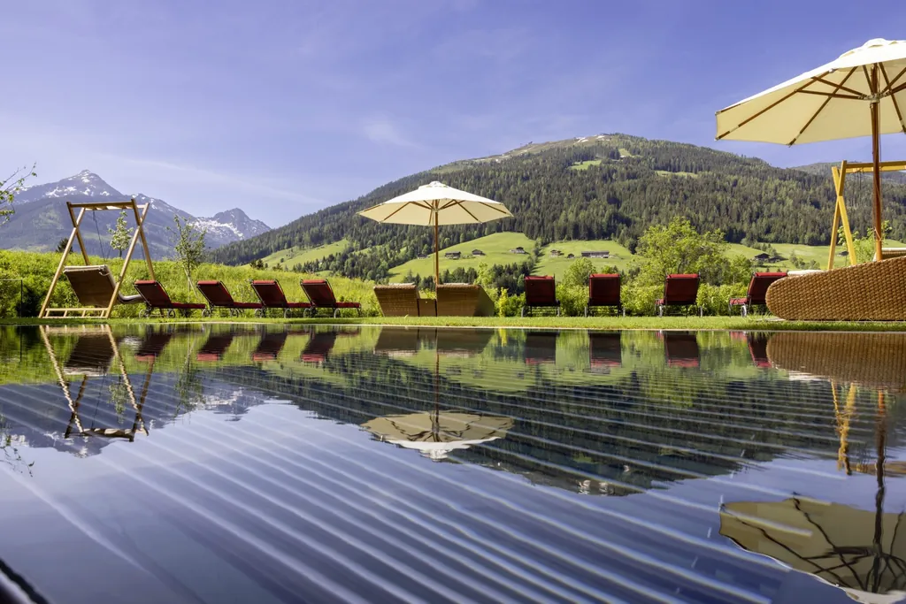 Outdoorpool mit roten Liegen am Rand und Blick auf die Berge im Mountain & Spa Resort Alpbacherhof