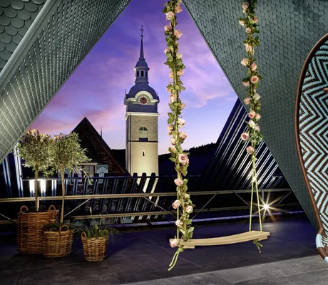 Blick auf die Bezauer Kirche mit Schaukel im Vordergrund auf dem Rooftop des GAMS zu zweit bei Abenddämmerung