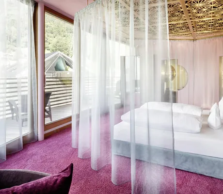 Blick in die Oh my God Suite mit grauem Himmelbett aus Samt, hellen Vorhängen und pinkem Teppichboden des GAMS zu zweit