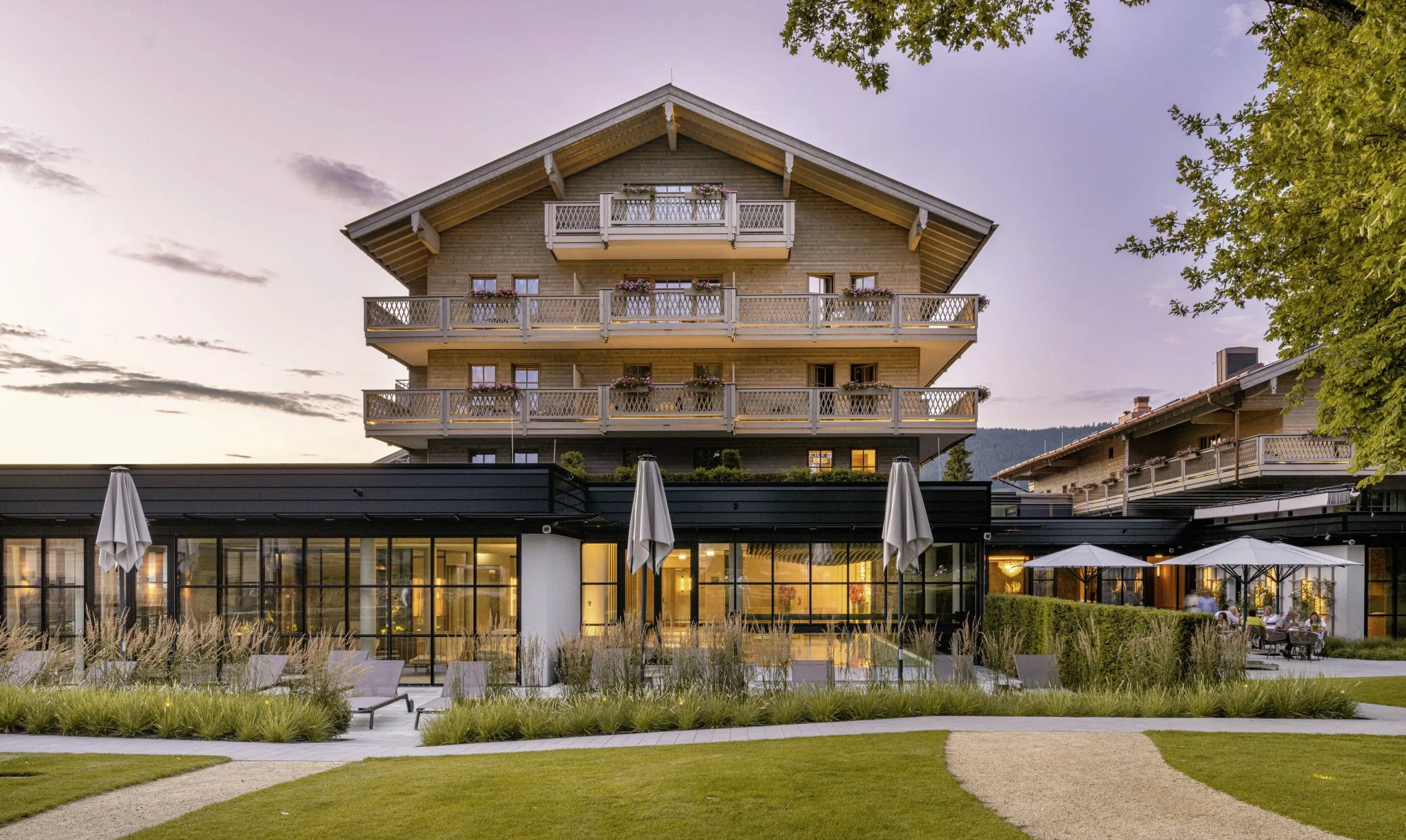 Rückansicht des Parkhotel Egerner Höfe mit rustikalem Haupthaus und Spagebäude mit schwarzem Stahl