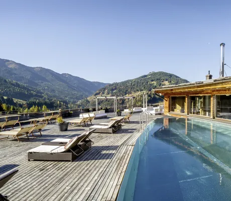 Rooftop-Pool des Holzhotel Forsthofalm mit Sonnenliegen und Bergen im Hintergrund