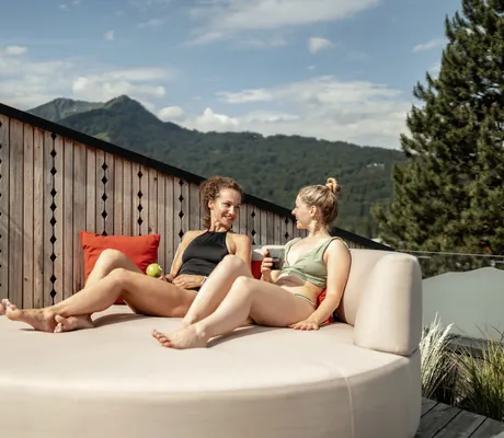 Zwei Frauen sitzen auf einer Liege im Outdoorbereich des Hotel Franks und lächeln sich an